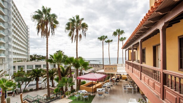 Un patio de hotel con asientos al aire libre, palmeras y vistas a la playa.