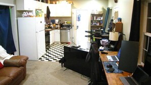 Una cocina compacta con microondas, estufa y refrigerador. Hay una zona de comedor con una mesa y sillas, y un escritorio con varios computadores portátiles.