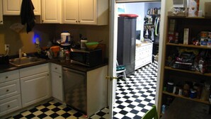 Una cocina con armarios blancos, un microondas y suelo a cuadros.