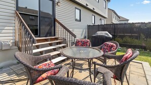 Une terrasse avec des meubles en osier et une table en verre, un escalier en bois et une clôture noire.