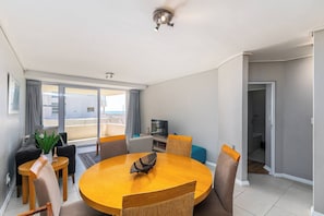 Un salon moderne avec une table ronde en bois, des sièges confortables, un téléviseur à écran plat et un balcon avec vue.
