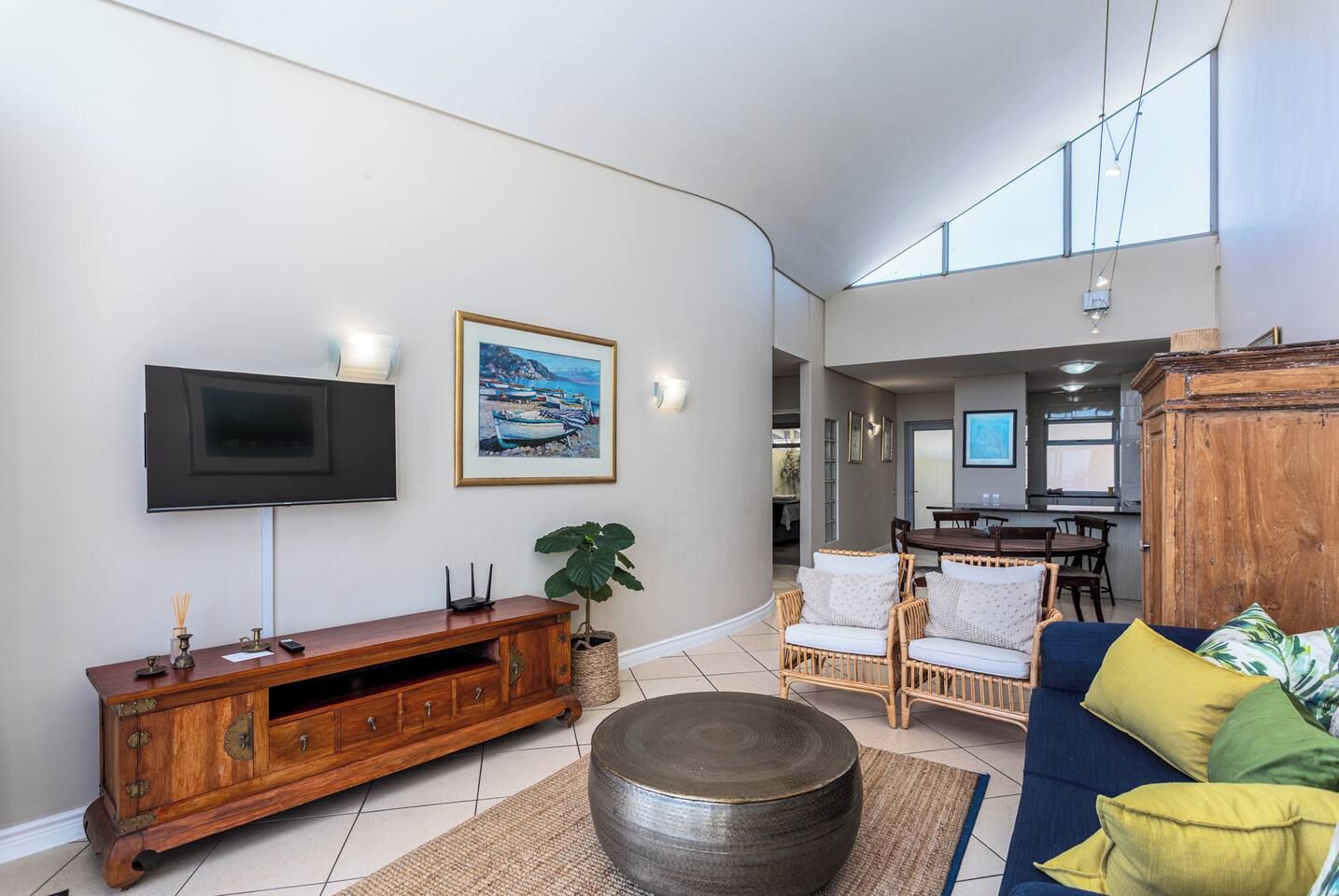 A modern living room with a flat-screen TV, a wooden entertainment unit, wicker furniture, and a large window.
