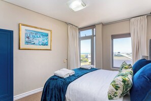 A bedroom with a bed, a window with a view, a door, and a framed picture on the wall.