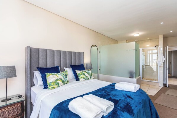 A hotel room with a bed, a nightstand, a lamp, a mirror, and a shower area.