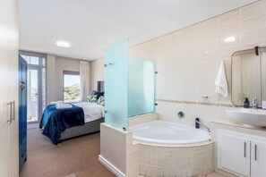 Una camera d'albergo moderna con un letto, cabina doccia in vetro, vasca da bagno e bagno con lavandino e specchio.
