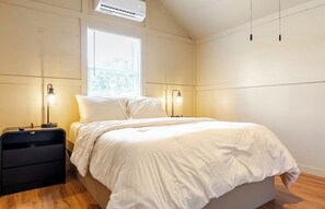 Ein Schlafzimmer mit einem Bett, zwei Nachttischen, einem Fenster und einer Klimaanlage.