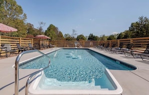 Une piscine rectangulaire avec un escalier en métal, entourée de chaises longues en bois et de parasols.