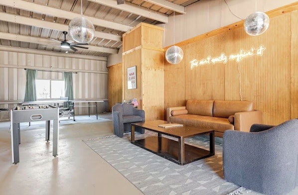 A spacious room with a wooden wall, a neon sign, a sofa, a coffee table, and a foosball table.