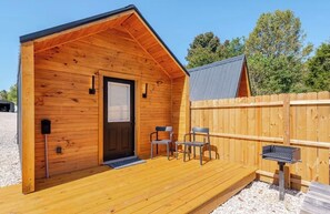Eine Holzhütte mit Veranda, einer Tür, zwei Stühlen und einem Grill.