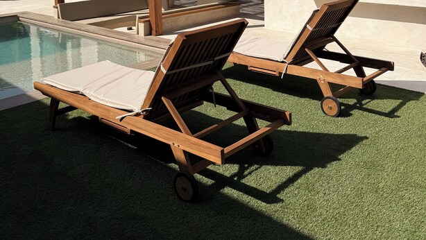 Uma área à beira da piscina com duas espreguiçadeiras de madeira e uma cobertura em pérgola.