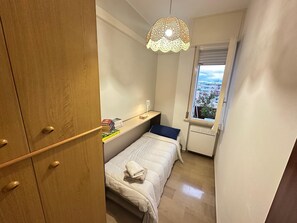 A small, well-lit bedroom with a bed, a bedside table with books, a window with a view, and a wooden wardrobe. - 'Between Sky and Sea by Vale' Apartment with Balcony and Air Conditioning (Fano)