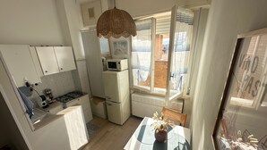 A compact kitchen with a microwave, stove, and refrigerator. There's a dining table with a vase of dried flowers. - 'Between Sky and Sea by Vale' Apartment with Balcony and Air Conditioning (Fano)