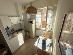 A compact kitchen with a microwave, stove, and refrigerator. There's a dining table with a vase of dried flowers.