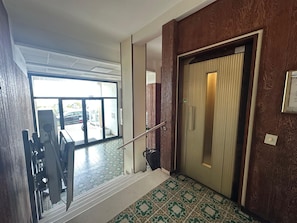 A staircase leading to a room with a patterned floor, a door with a vertical handle, and a view of the outside through a glass door.