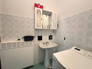 A bathroom with a white sink, a mirror above it, a white toilet, and a white heater unit. - 'Between Sky and Sea by Vale' Apartment with Balcony and Air Conditioning (Fano)
