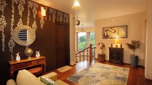 A spacious living area with a wooden floor, a large mirror, a sofa, a decorative wall, and a staircase leading to a balcony.