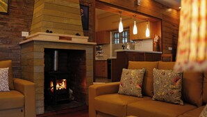 A cozy living room with a fireplace, a sofa with floral cushions, and a kitchen area in the background.