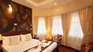 A hotel room with a large bed, a wooden headboard, a nightstand, a lamp, a chair, and a window with curtains.