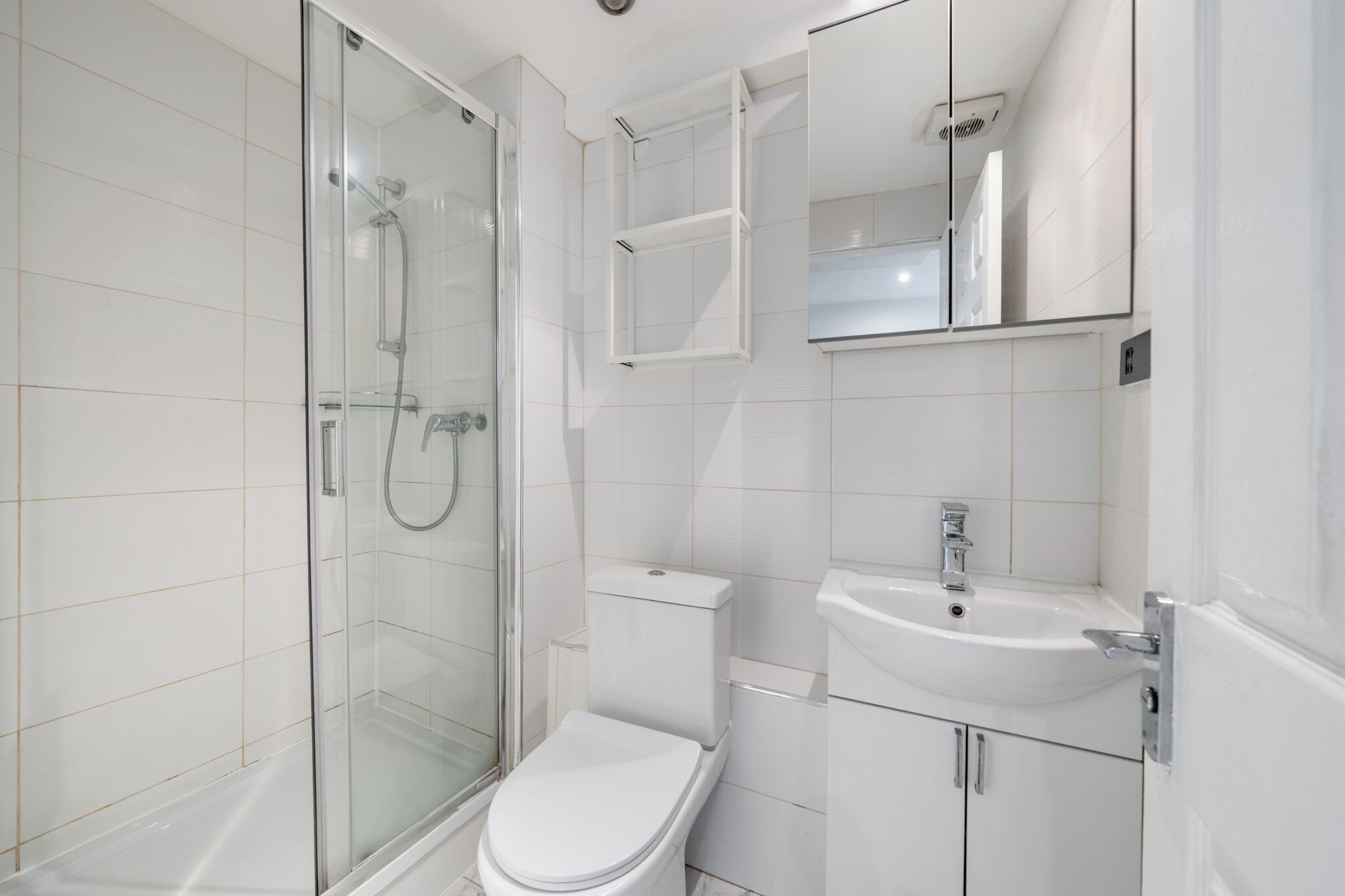 A modern bathroom with a glass-enclosed shower, a white toilet, and a sink with a mirror above it.