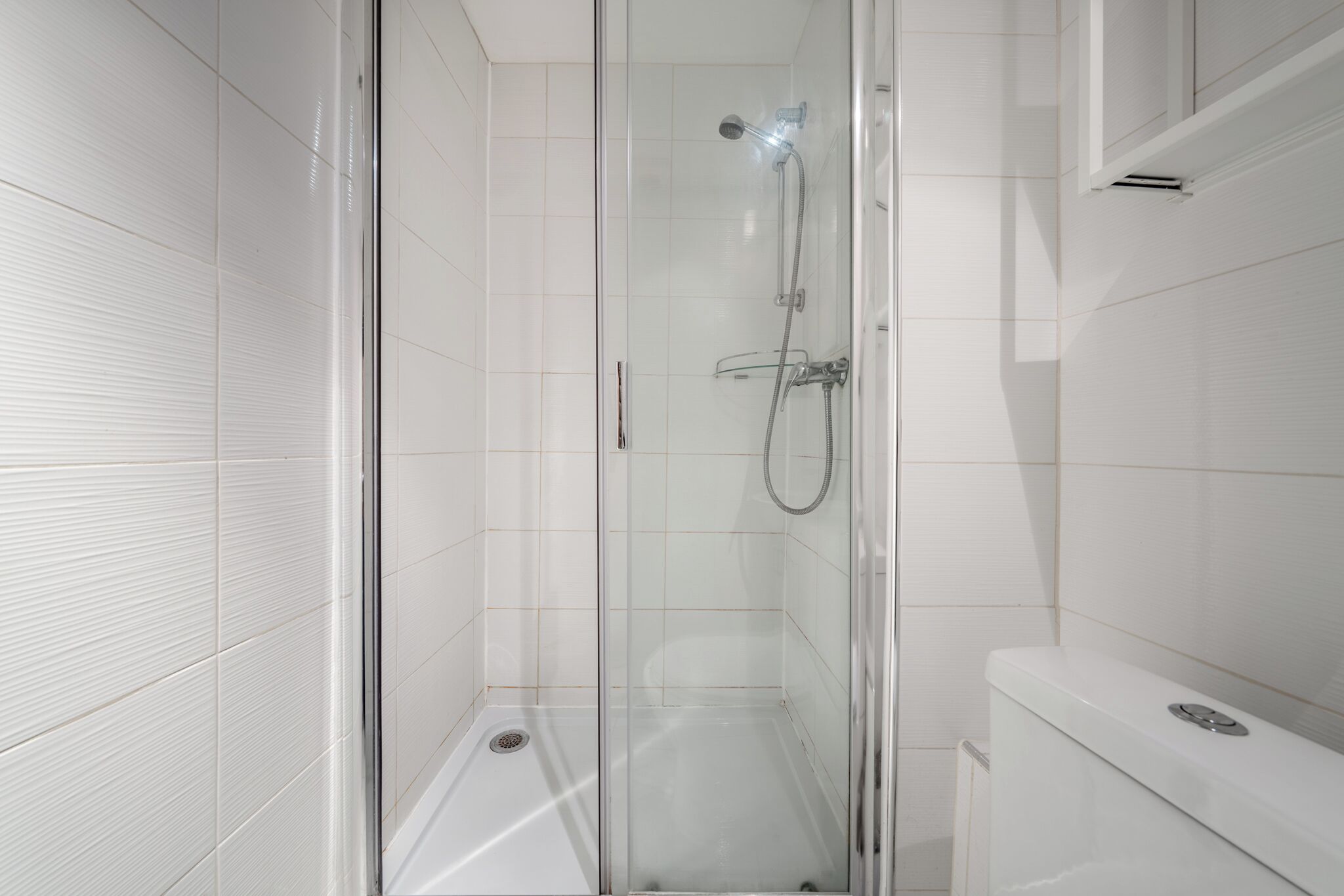 Een moderne badkamer met een douchecabine van glas, witte betegelde wanden en een wit toilet.