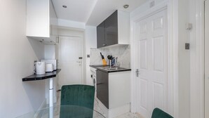 A compact kitchen with a built-in washing machine, a glass dining table, and a green chair.