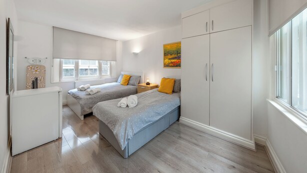 A modern bedroom with two beds, a wardrobe, and a small desk.