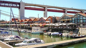 Una marina con barche ormeggiate, un ponte sopra e un edificio con posti a sedere all'aperto.