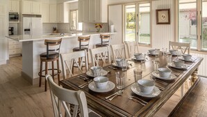 A spacious kitchen with white cabinetry, a central island with bar stools, and a dining area set for six with a wooden table and white plates. - Fairway Views | Ski Trail | Hot Tub (Big Sky)