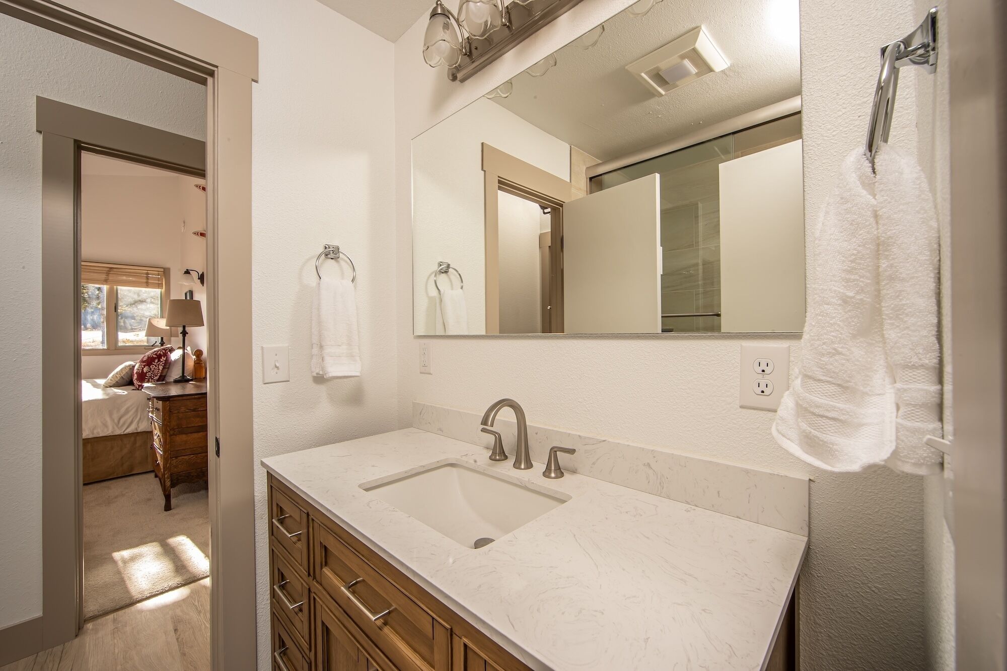 A bathroom with a double sink, wooden cabinets, a mirror, and a towel rack.