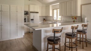 A modern kitchen with white cabinetry, a large island with bar stools, and a painting on the wall. - Fairway Views | Ski Trail | Hot Tub (Big Sky)