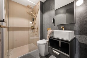 A modern bathroom with a glass-enclosed shower, a white toilet, and a black vanity with a mirror.