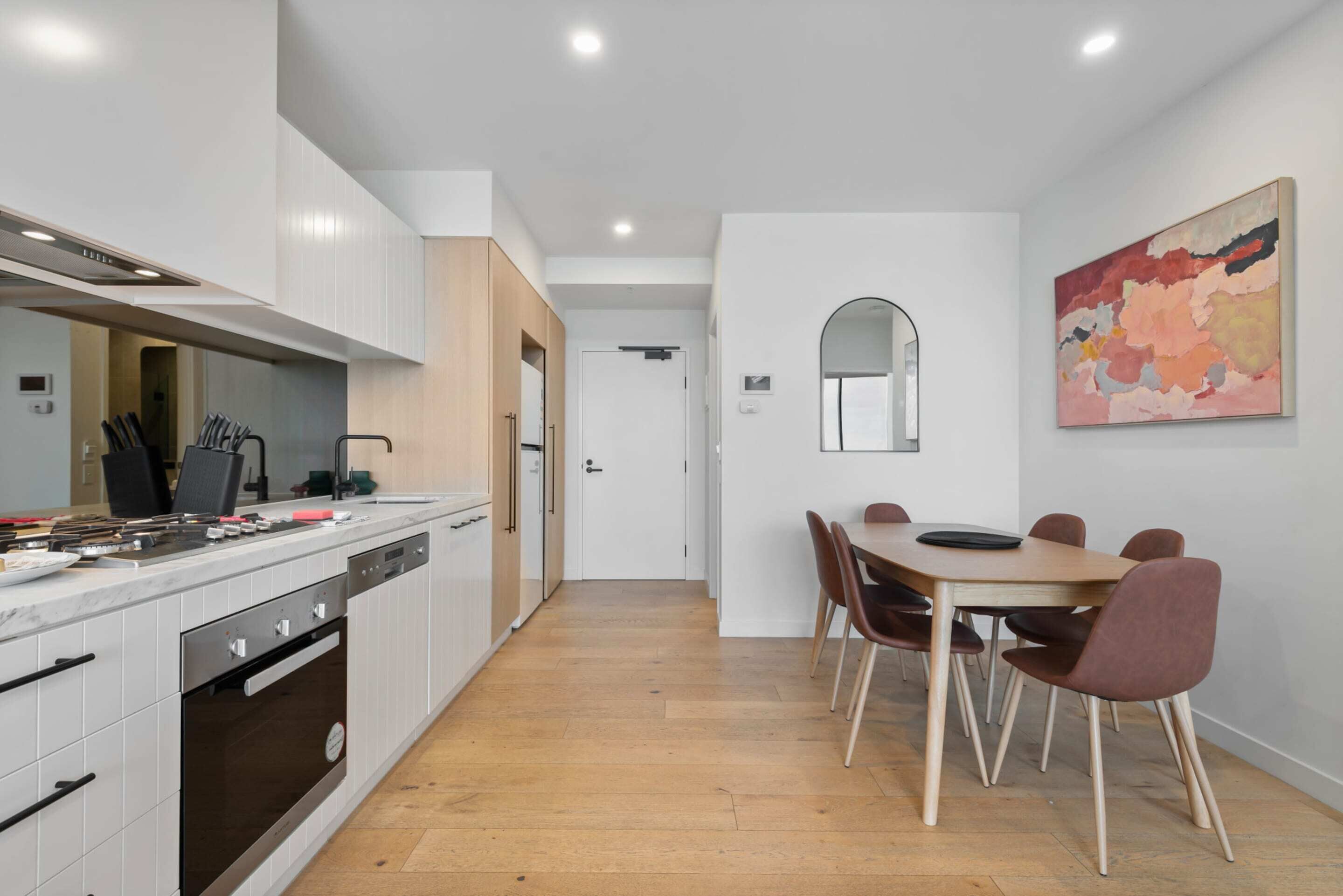 A modern kitchen with white cabinets, a built-in oven, and a dining area with a wooden table and chairs.