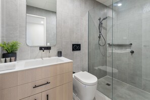 A modern bathroom with a wooden vanity, a toilet, a glass shower enclosure, and a mirror.
