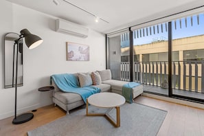 Un salon moderne comprenant un canapé, une table basse ronde, un lampadaire et une grande porte-fenêtre coulissante donnant sur un balcon extérieur.