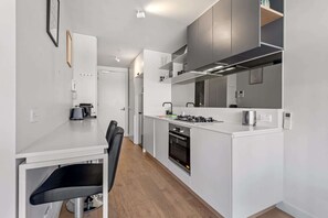 A modern kitchen with white cabinetry, a built-in oven, and a dining area with a chair.