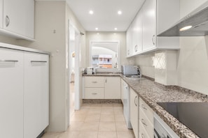 A narrow kitchen with white cabinets, a granite countertop, and a view to the outside.