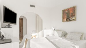 Ein Hotelzimmer mit einem Bett, einem Schreibtisch mit Laptop, einem Sessel, einem Fernseher und einem Bild an der Wand.