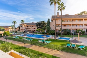 A hotel with a swimming pool, palm trees, and a well-maintained lawn.