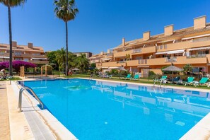 Une piscine avec des chaises longues, des palmiers et un bâtiment doté de balcons.