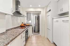 A modern kitchen with white cabinetry, granite countertops, stainless steel appliances, and a central island with fruits and vegetables.