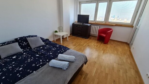 Een slaapkamer met een bed, een televisie, een rode stoel en een raam met uitzicht op de stad.
