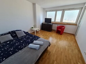 A bedroom with a bed, a TV, a red chair, and a window with a city view. - Fantastic Inn Warsaw - Świętokrzyska (Warsaw)