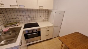 Een compacte keuken met witte kastjes, een ingebouwde oven, een spoelbak en een kleine koelkast.
