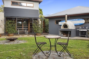 A patio with a stone fire pit, two metal chairs, and a small table. - Stylish 3-bedroom and Outdoor Grill and Pizza Oven (Drysdale)
