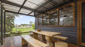 A wooden deck with a table and benches, a pergola with string lights, and a view of the surrounding landscape. - Stylish 3-bedroom and Outdoor Grill and Pizza Oven (Drysdale)