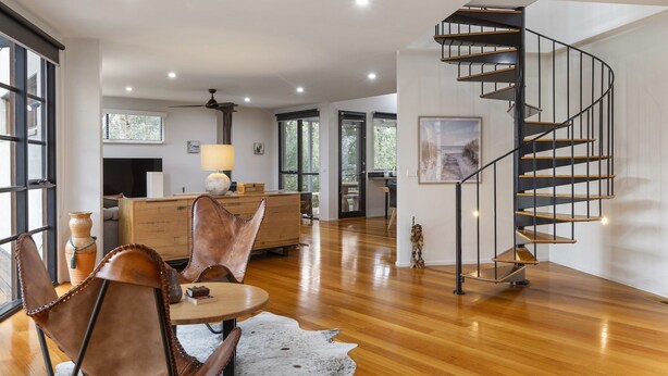 A spacious living area with a wooden floor, a round table, leather chairs, a sofa, and a spiral staircase. - Stylish 3-bedroom and Outdoor Grill and Pizza Oven (Drysdale)