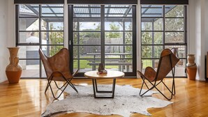 A room with a large sliding glass door leading to an outdoor patio, two leather chairs, a round table, and a cowhide rug. - Stylish 3-bedroom and Outdoor Grill and Pizza Oven (Drysdale)