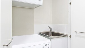 A compact laundry room with a front-loading washing machine, a built-in dryer, and a stainless steel sink. - Madecomfy Spacious Canberra LI (Canberra)