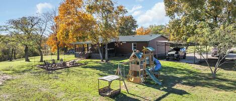 A wooden cabin with a deck, a play structure, and a stone wall.