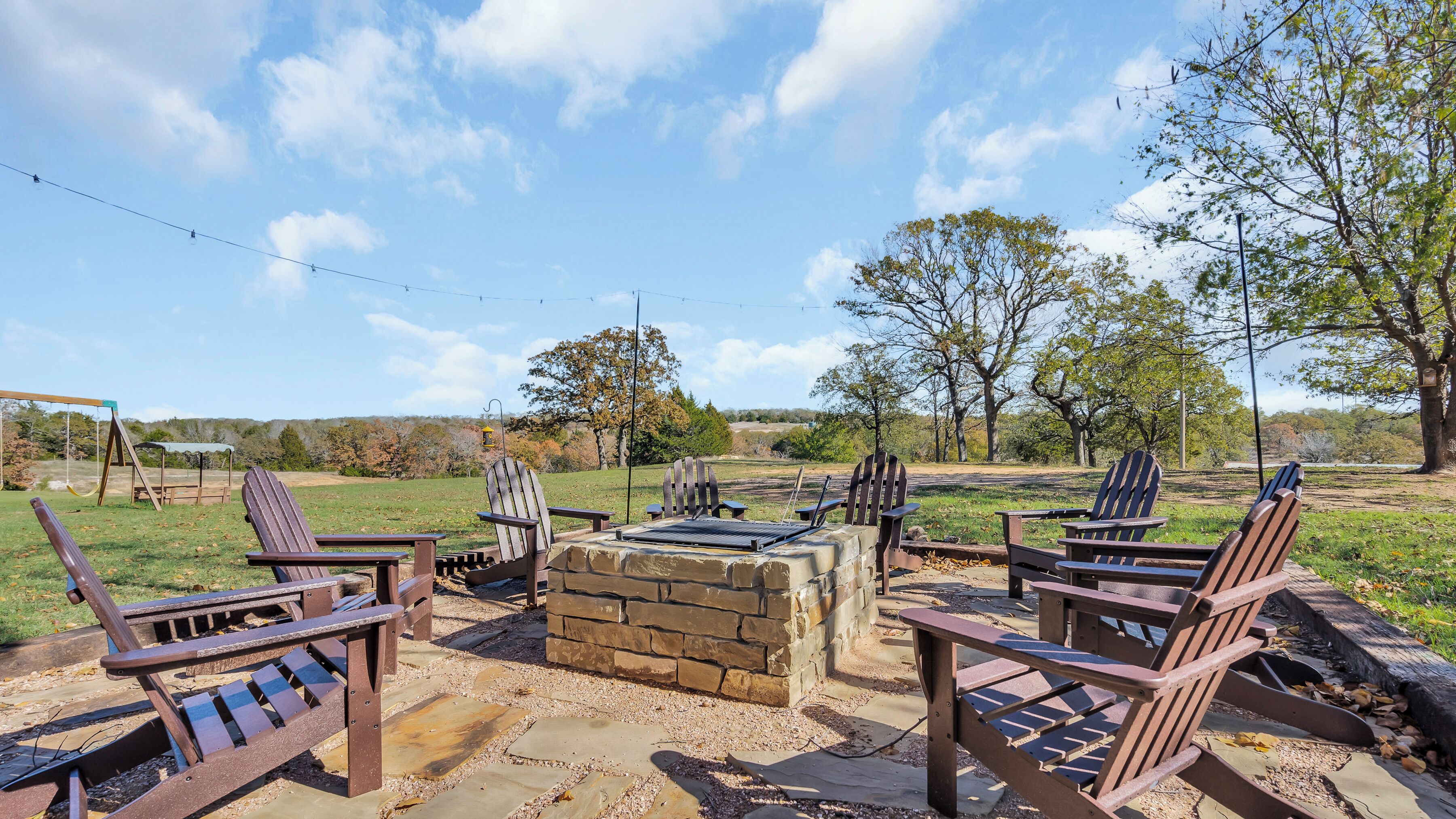 Un patio con sillas Adirondack, una chimenea y un columpio.